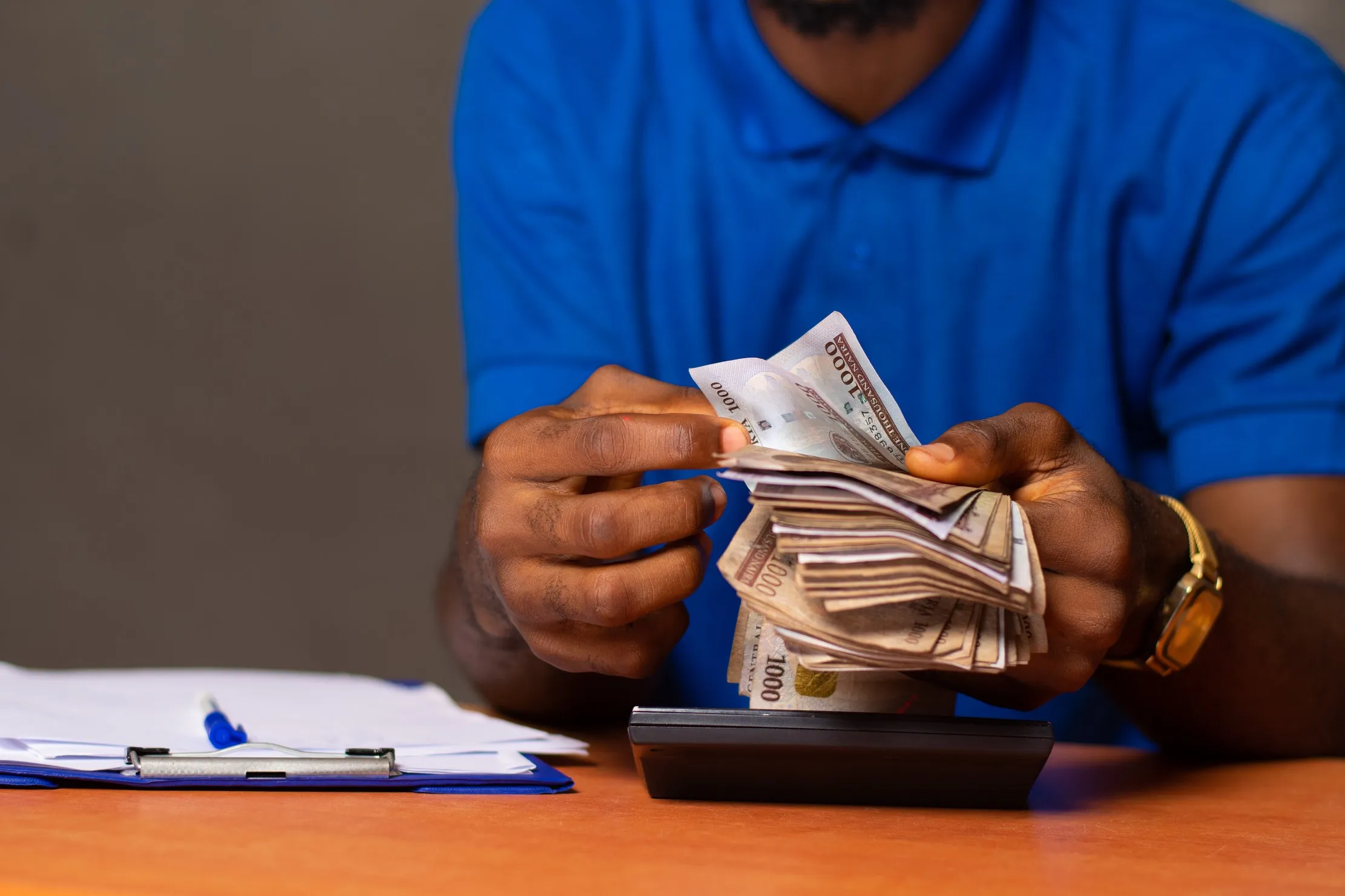 Une personne compte des billets près d’une calculatrice et d’un porte-documents ; ces billets ne représentent pas les opérations fictives en UM de ce guide.