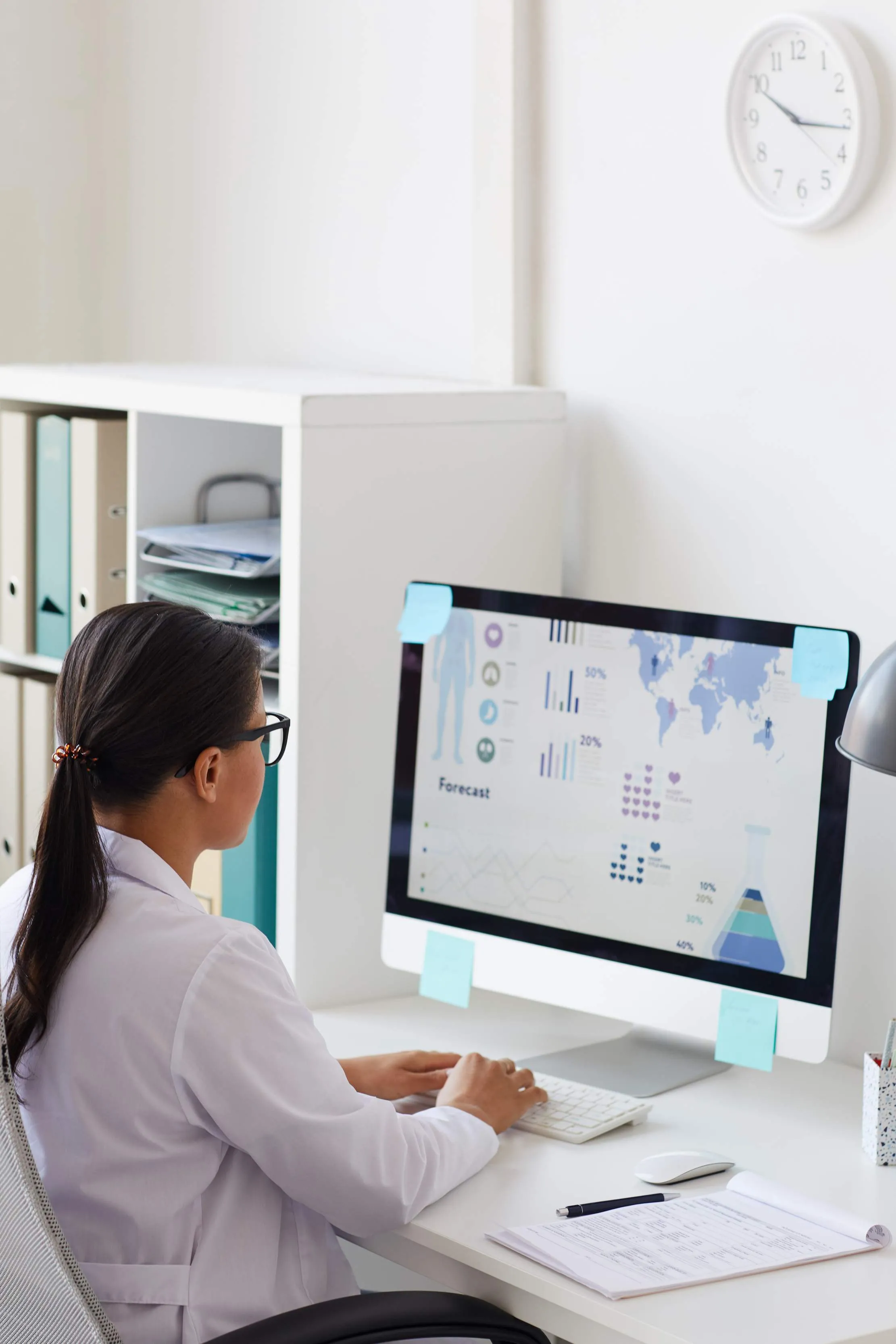 Réceptionniste de santé à un poste de travail informatique, illustrant la révision de l'enregistrement des patients et de la transmission de la file d'attente