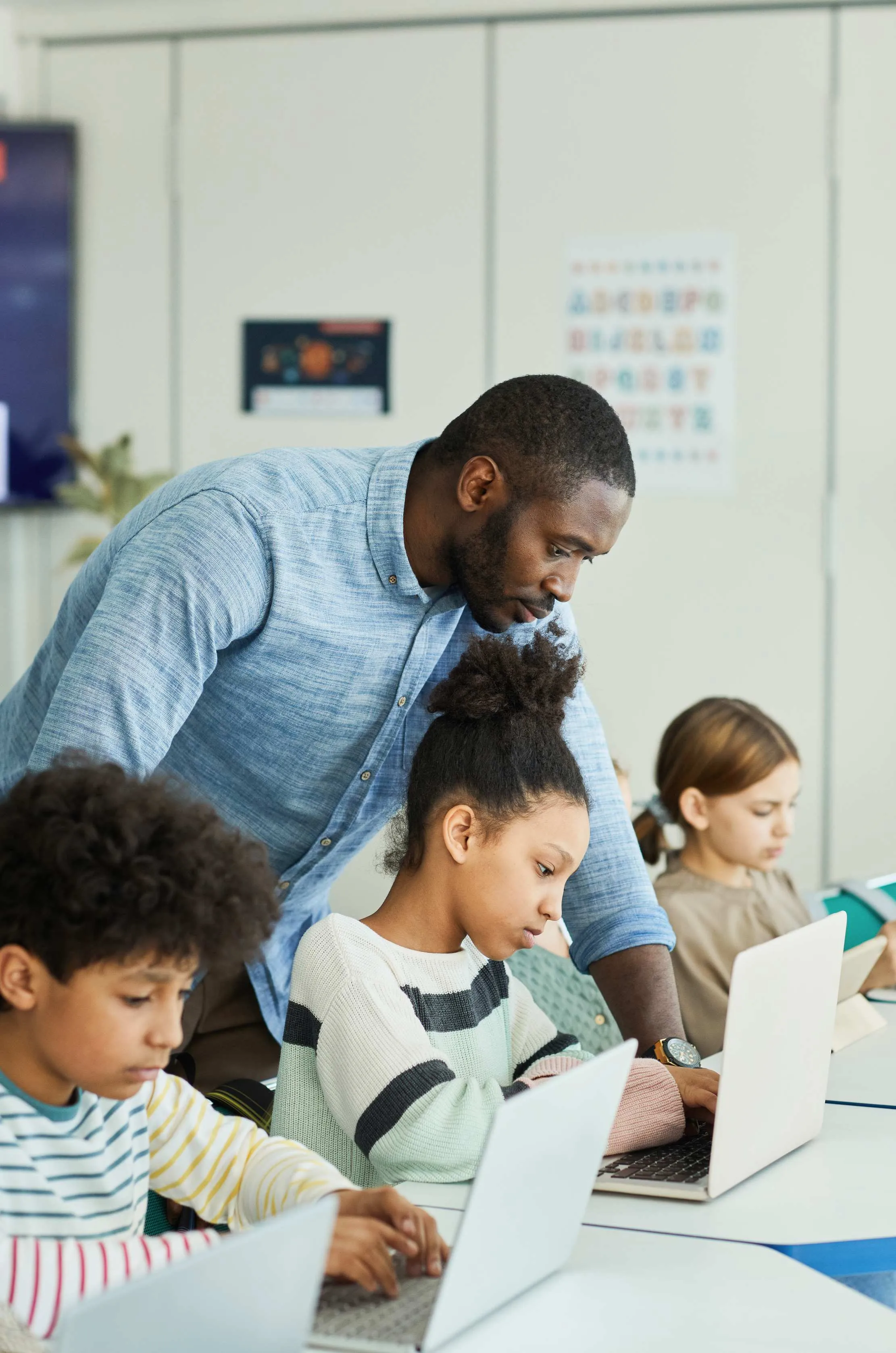 Teacher helping children on laptops in a classroom, representing checking roles, training, and support with the people who will actually use the system