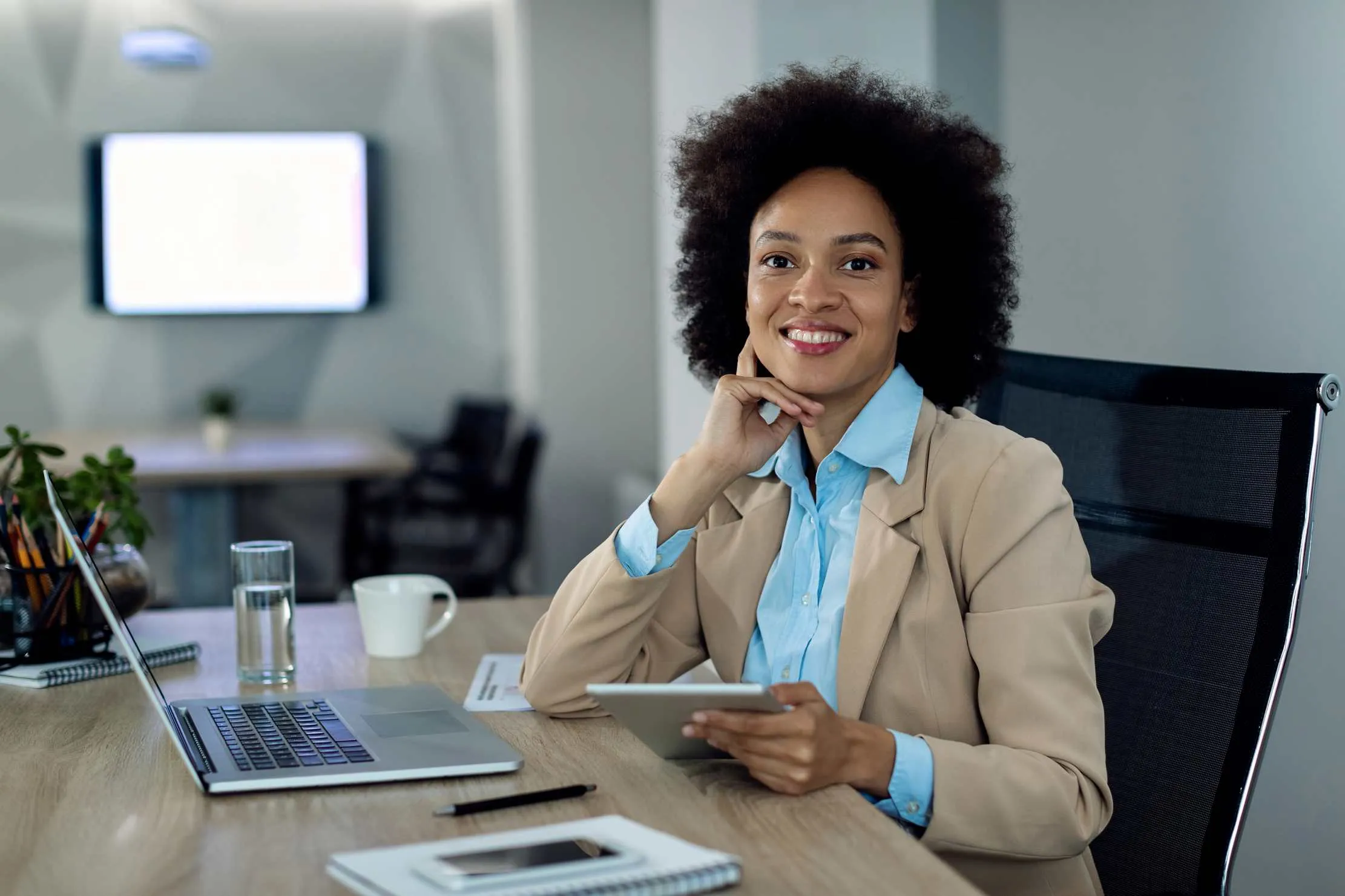 African professional woman working on tablet in office, representing the corporate employee who builds a side hustle